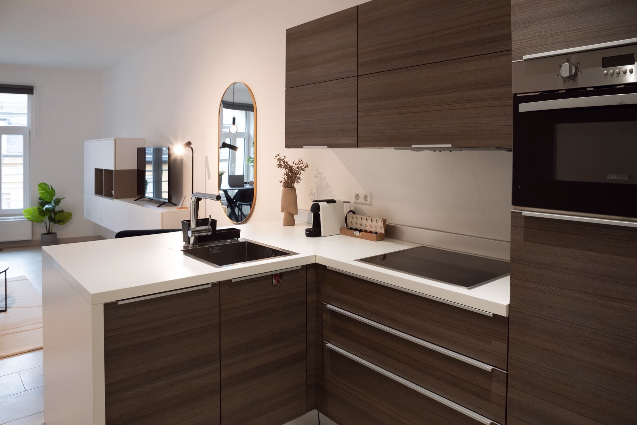 Fully equipped kitchen with mirror in the back and a TV stand with a smart TV on it. In the right corner, floor-to-ceiling window.