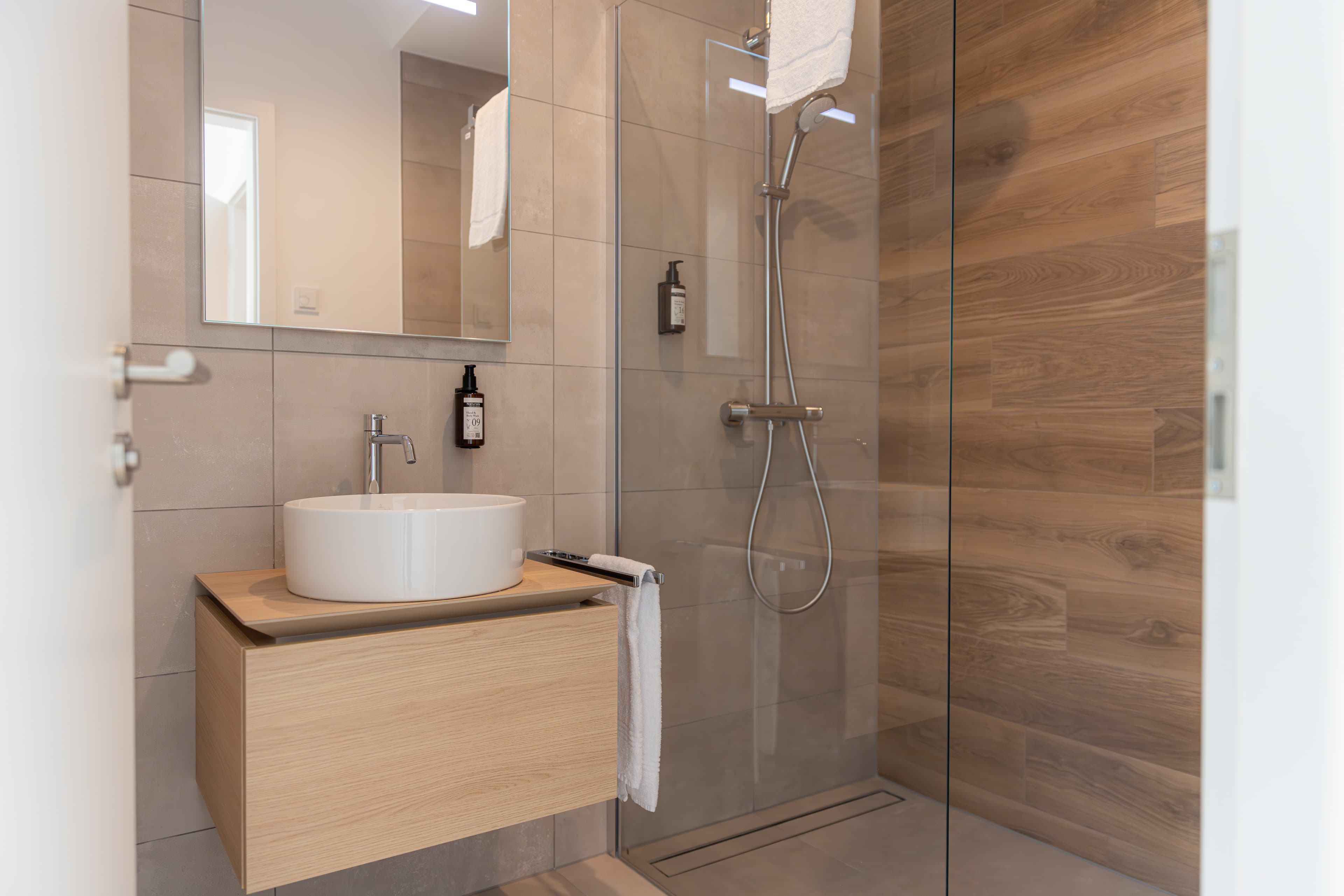 Overview of the bathroom with a walk-in shower, an oval sink and a large mirror above the sink.
Towels and hygiene products are available