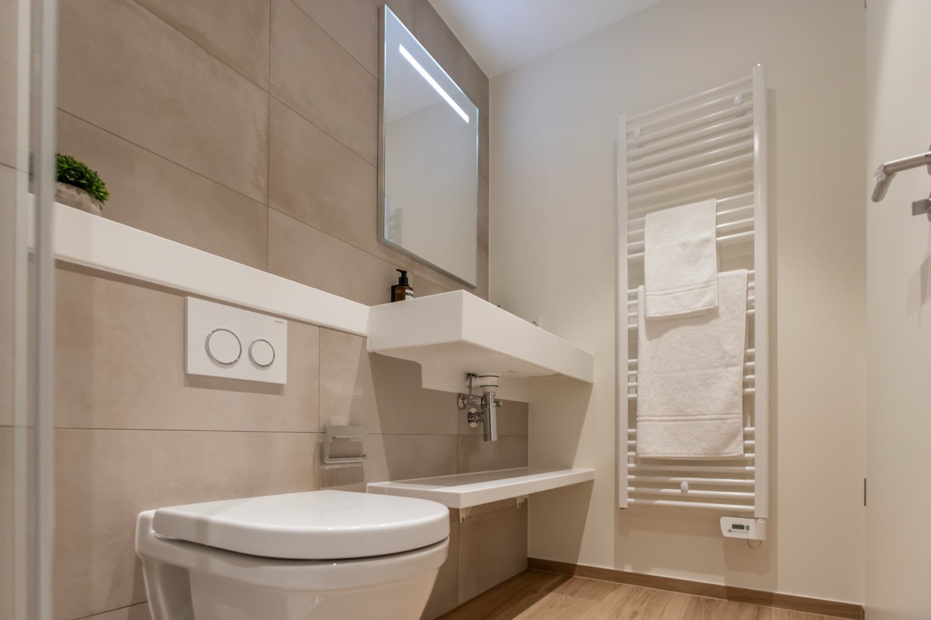 Bathroom corner with sink, mirror above, heating radiators and high-quality towels