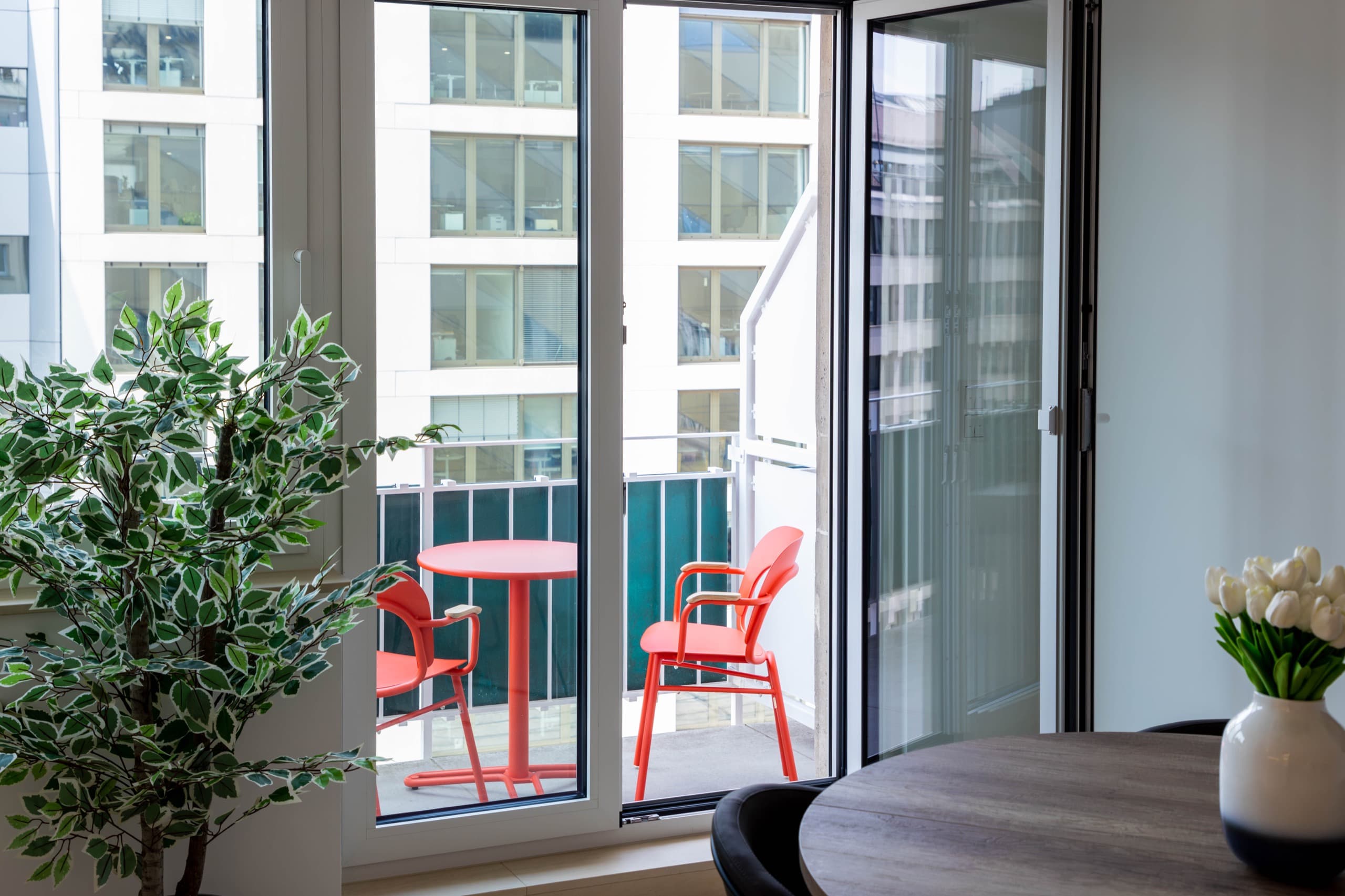 Balcony view through the lounge balcony door. It has a red round table and two red chairs.