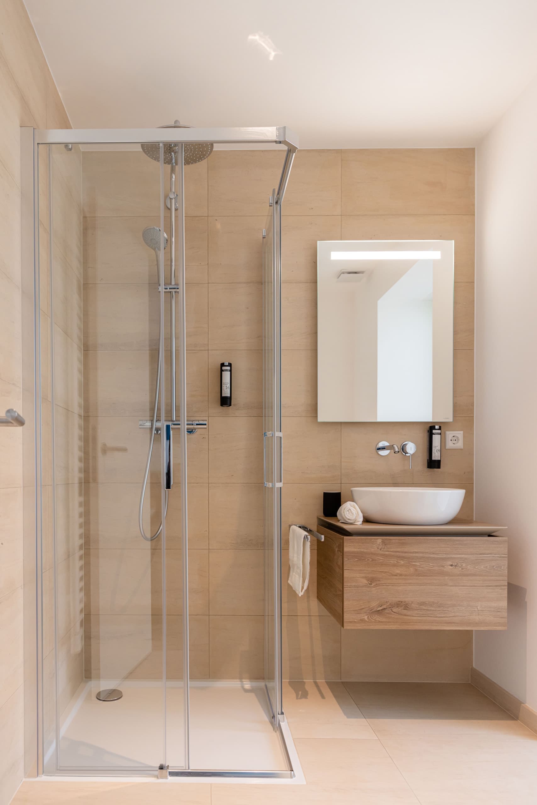 Bathroom with shower cabin, sink and mirror. Next to the sink, there are white towels and soap.
