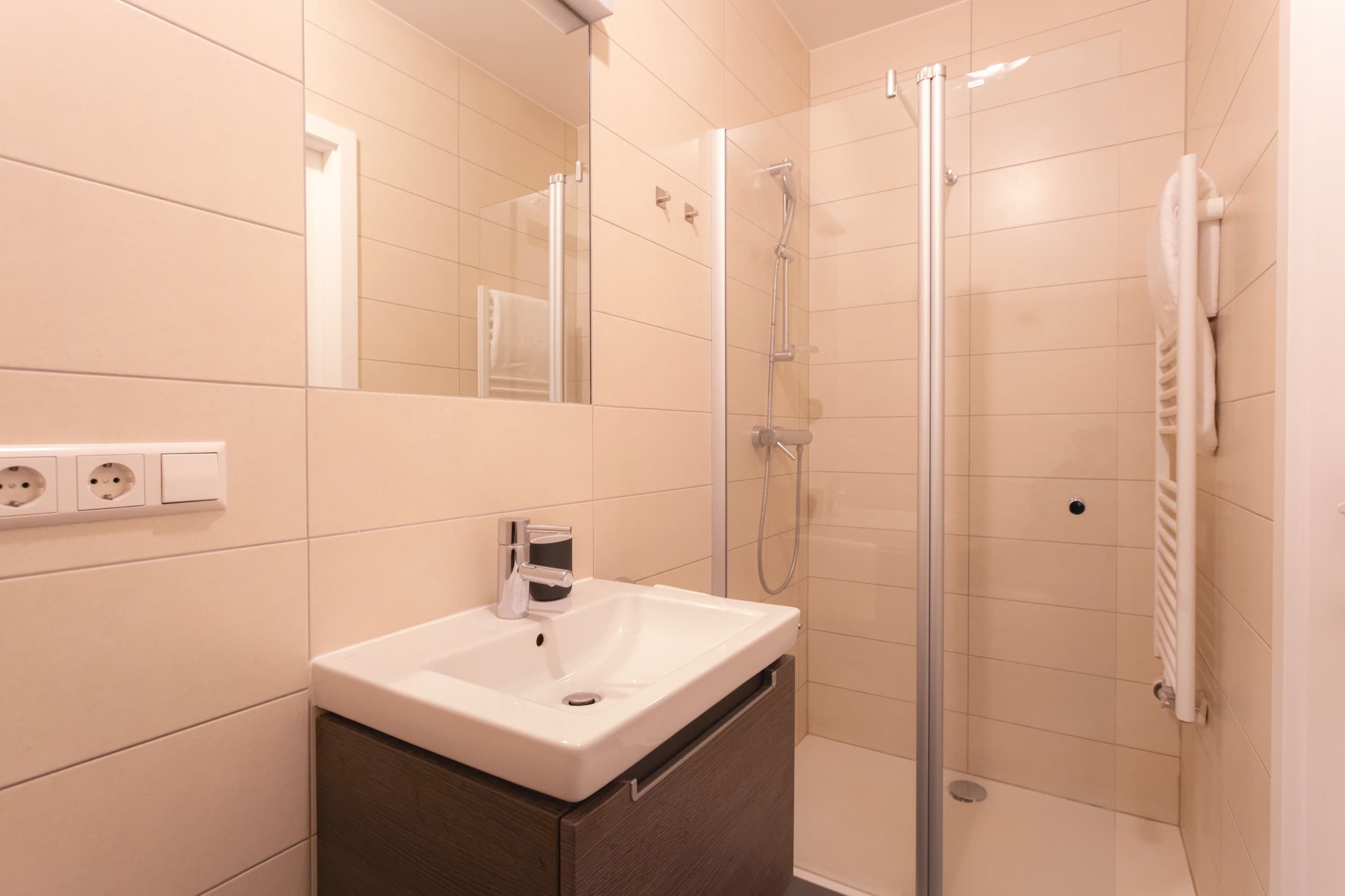 Bathroom with walk-in shower cabin and a white sink next to it. A mirror is above the sink. Soap and towels are provided.