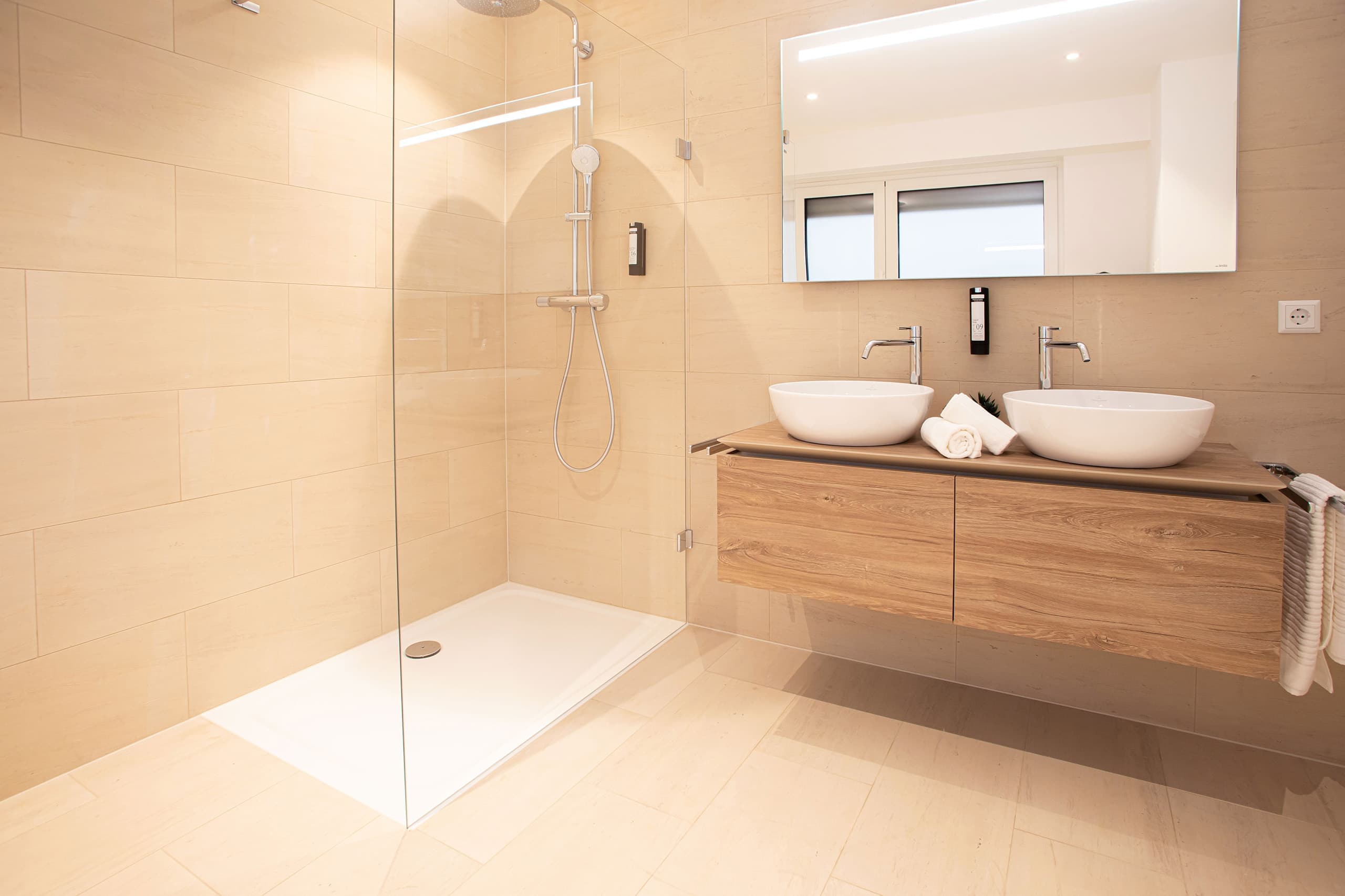 Bathroom with large walk-in shower cabin, and two sinks one next to the other. Above the sinks, there is a cabinet with mirror doors. Towels and soap are provided.
