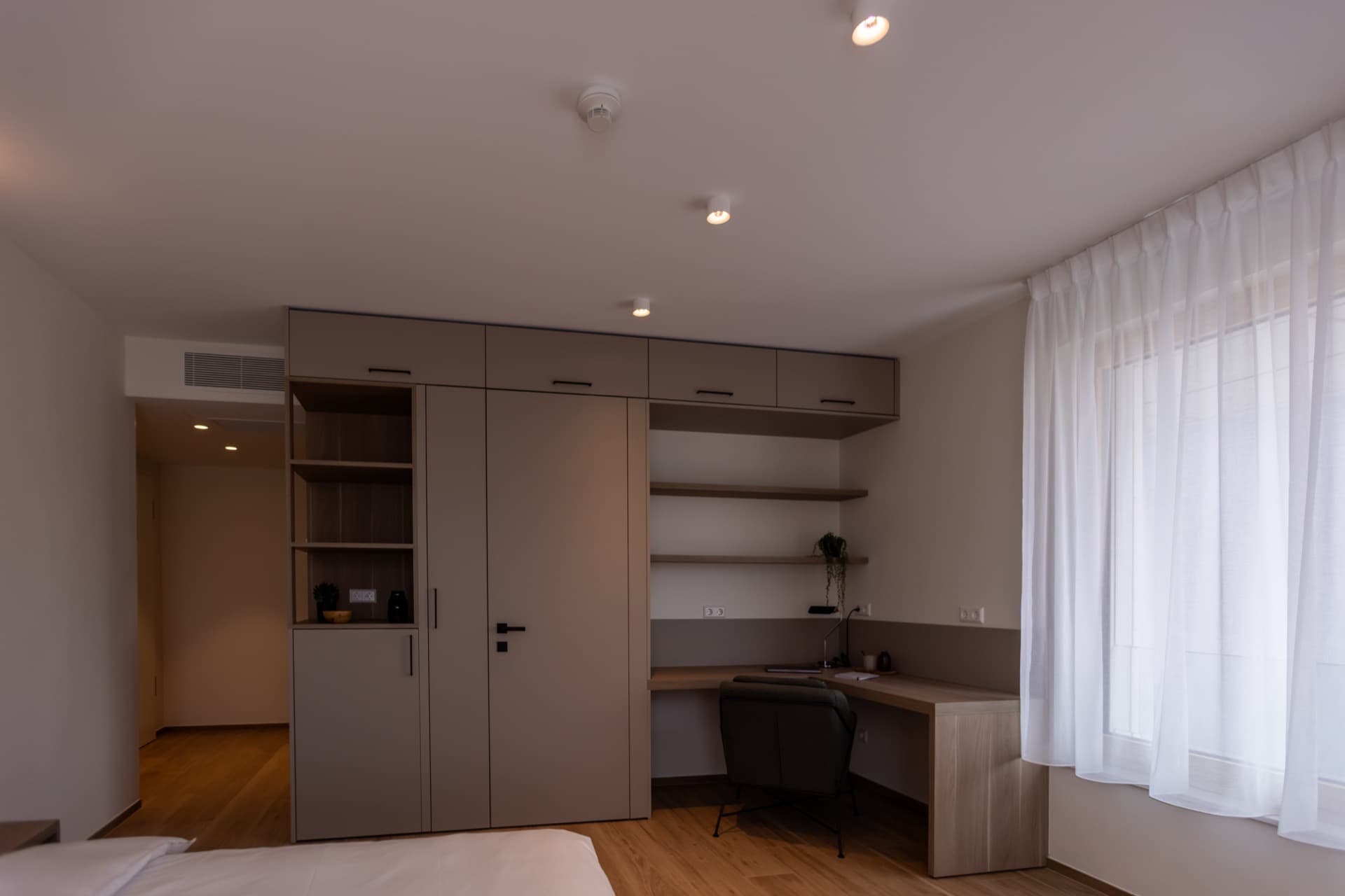 Working Area of the bedroom. It has a corner desk with a lamp, storage drawers and a small biblioteque. In on the wall of the desk there are plugs and light switches