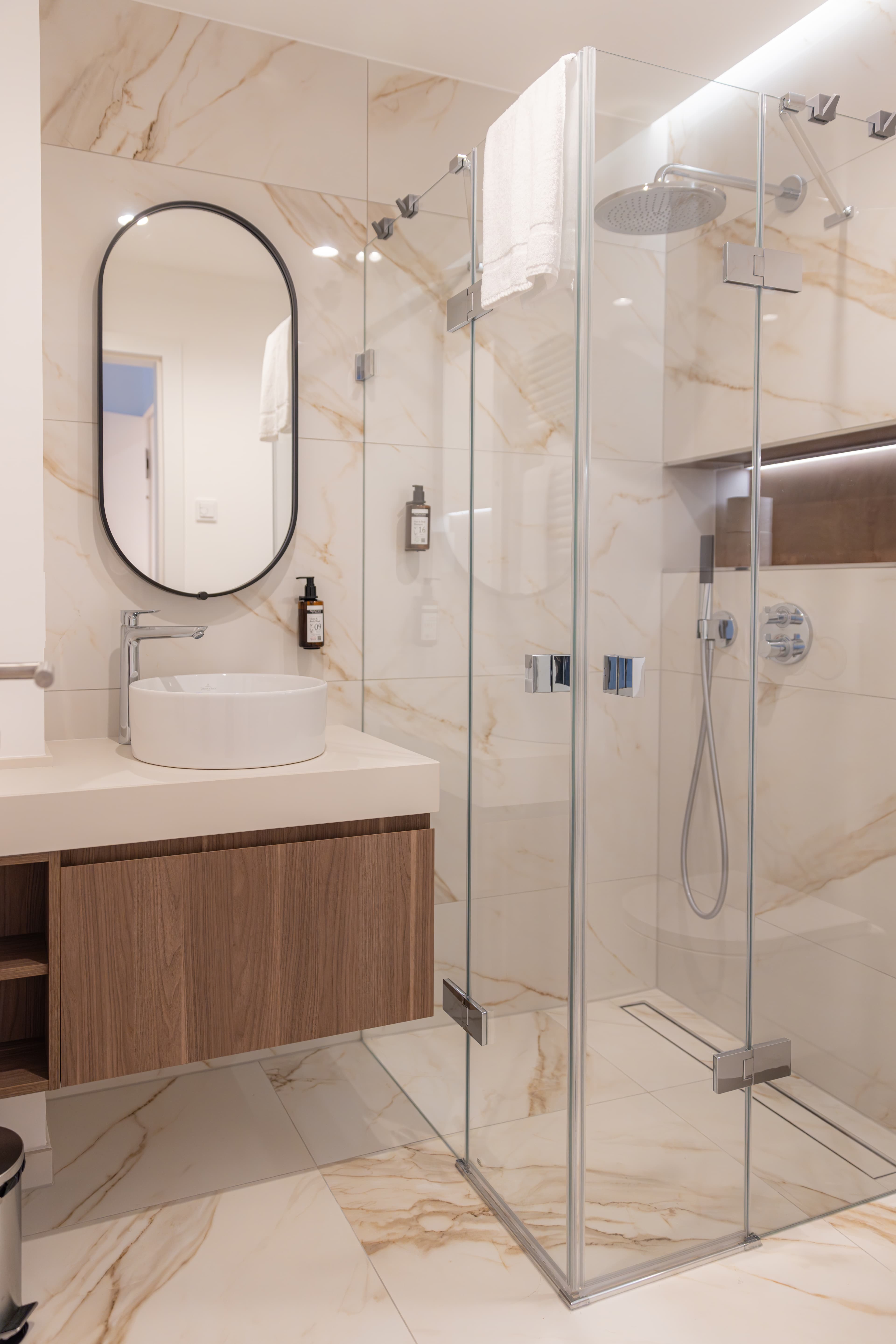 Bathroom with a walk-in shower, sink, and deposit drawers.A big mirror hangs on the wall. Soap, shower gel, and shampoo are in the bathroom.