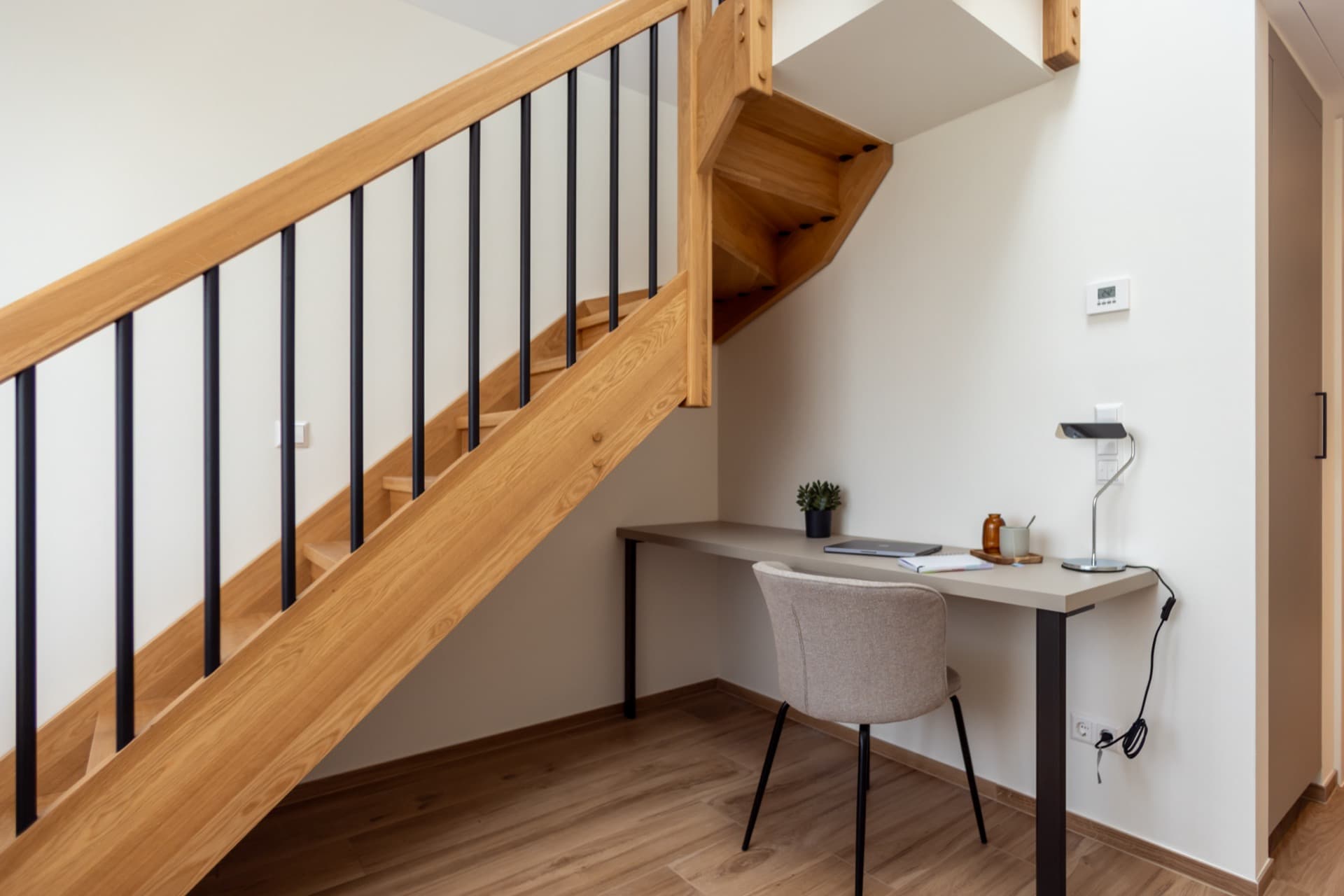 The picture depicts the working area of a furnished double bedroom for rent. It contains a desk, a comfortable chair, and a table lamp