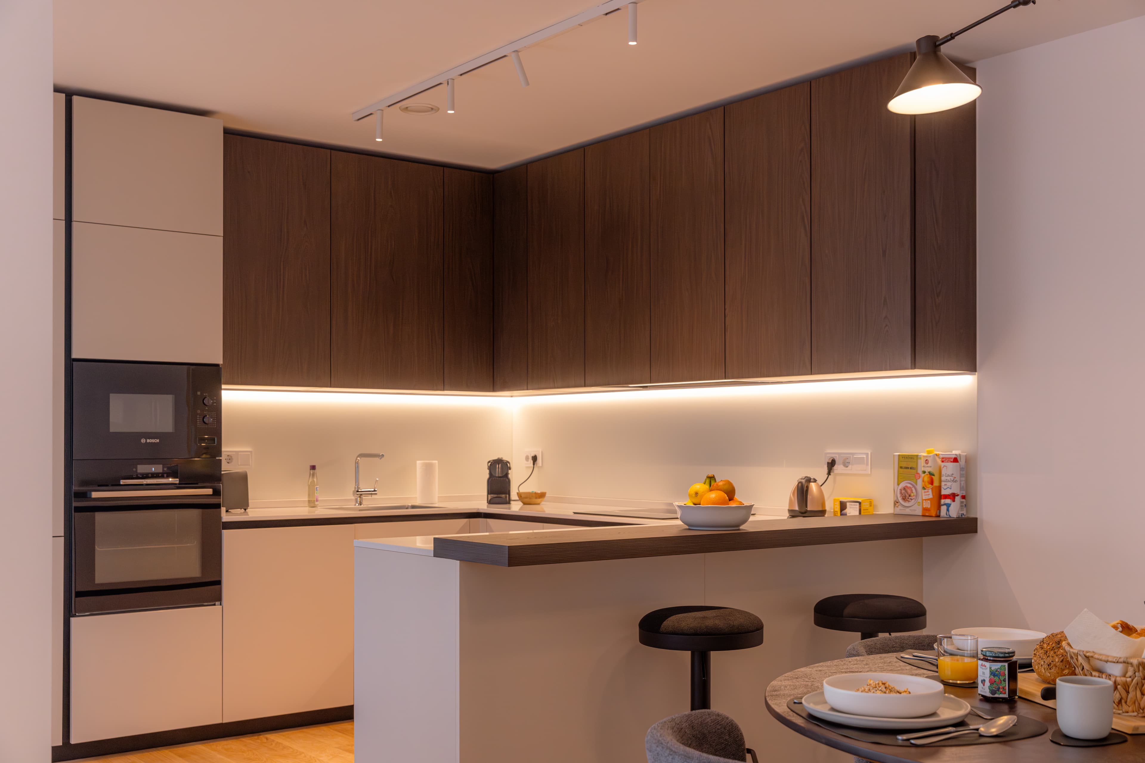 Overview of the fully equipped kitchen. It contains a stove, oven, a toaster, a kettle, and spacious storage drawers.
Next to it, there is a dining table in the dining area, with cutlery and silverware.