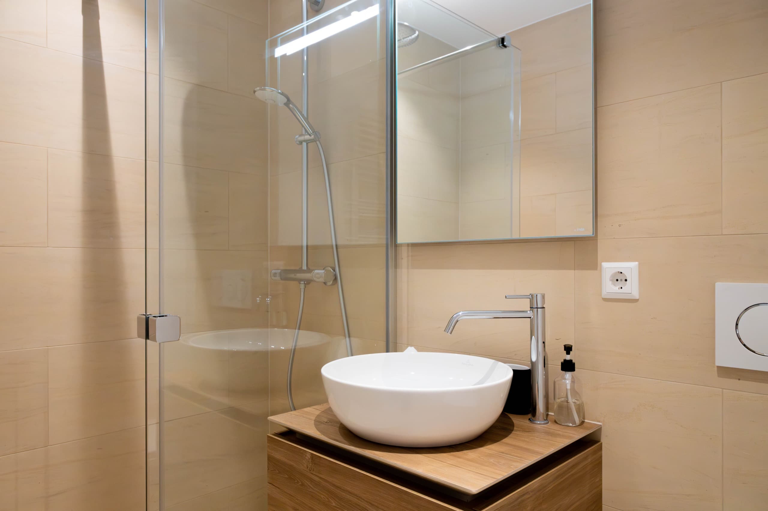 Walk-in shower cabin and white sink. Above the sink, there is a cabinet with mirror doors. Soap and towels provided