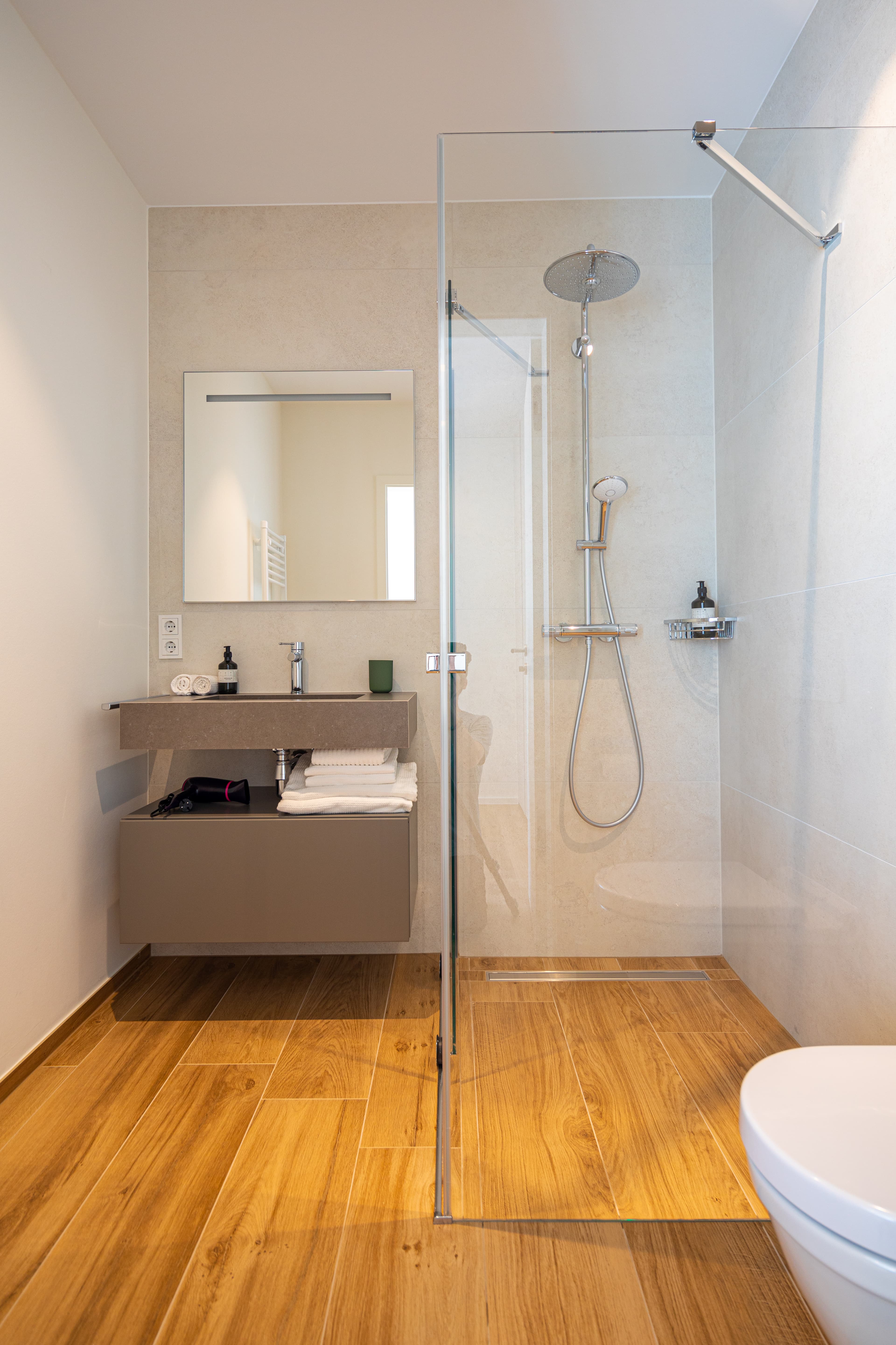 Bathroom with walk-in shower cabin and sink. Above the sink, a cabinet with mirror doors, bellow it, towels. Amenities included