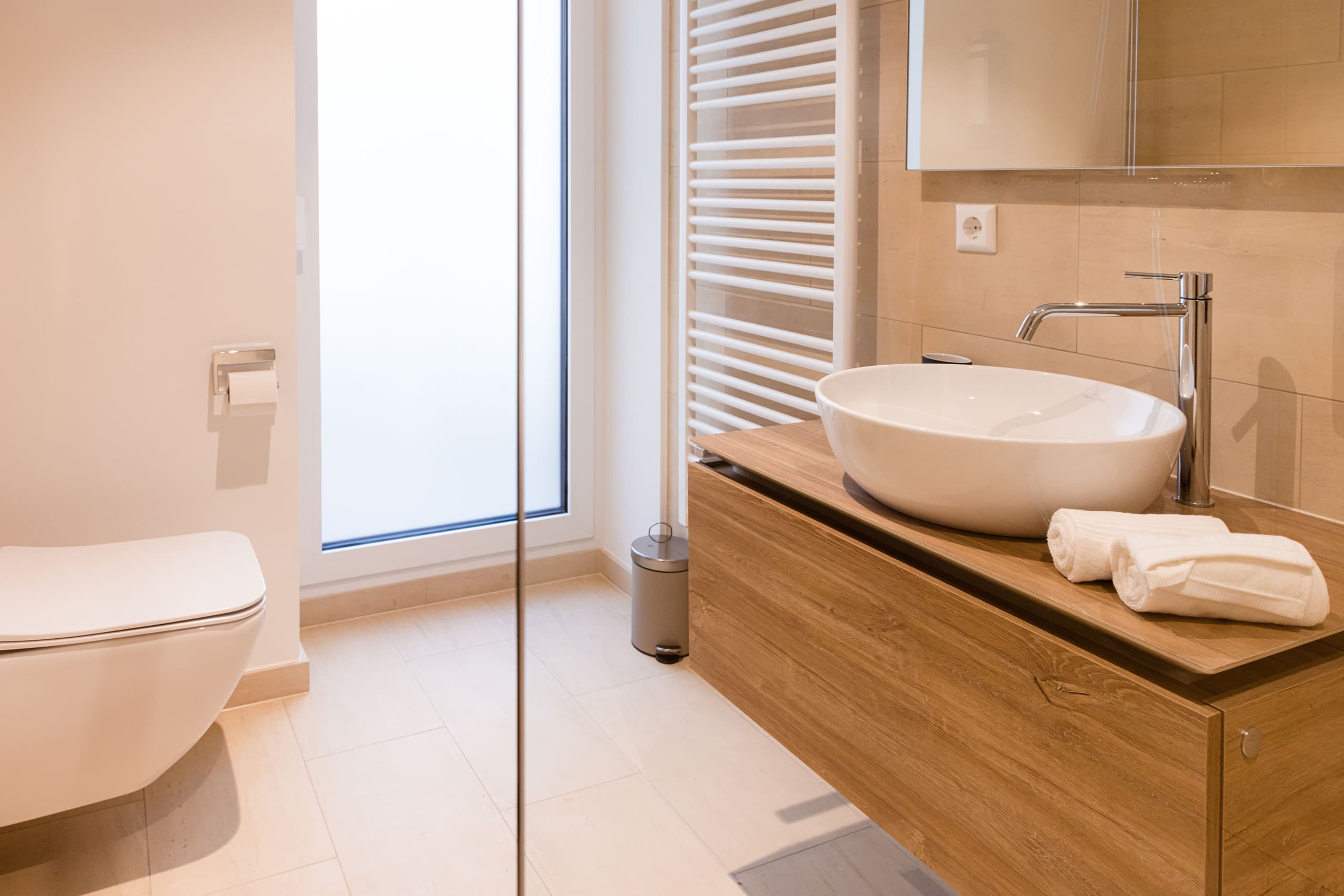 Bathroom with toilet, shower cabin, and a sink. Soap and towels provided. Behind the toilet, there is a big floor to ceiling window leading to a balcony.