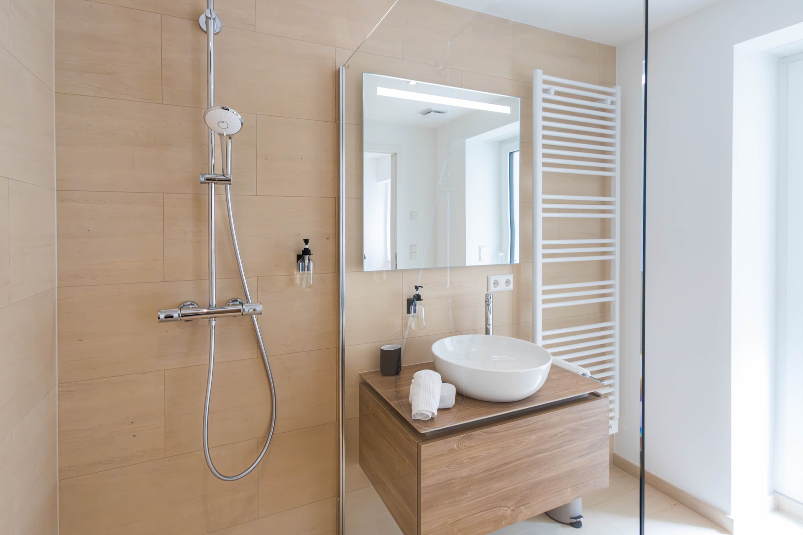 Bathroom with shower cabin and a sink next to it. Above the sink, there is a cabinet with mirror doors. On its right, there is a heating radiator.