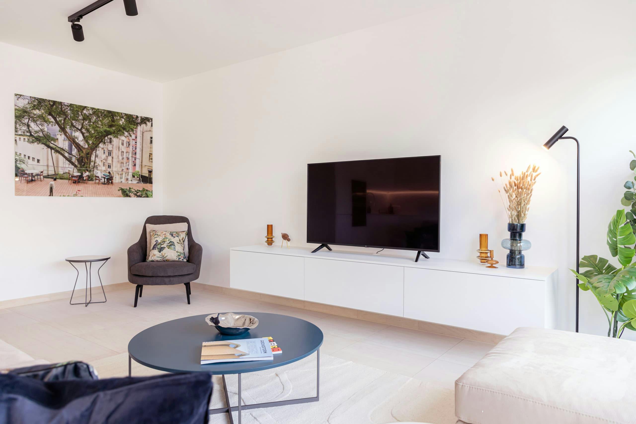 Living area of Apartment Alzette at Hamilius Apartments showing an armchair, television unit with smart TV and vases with dried flowers.