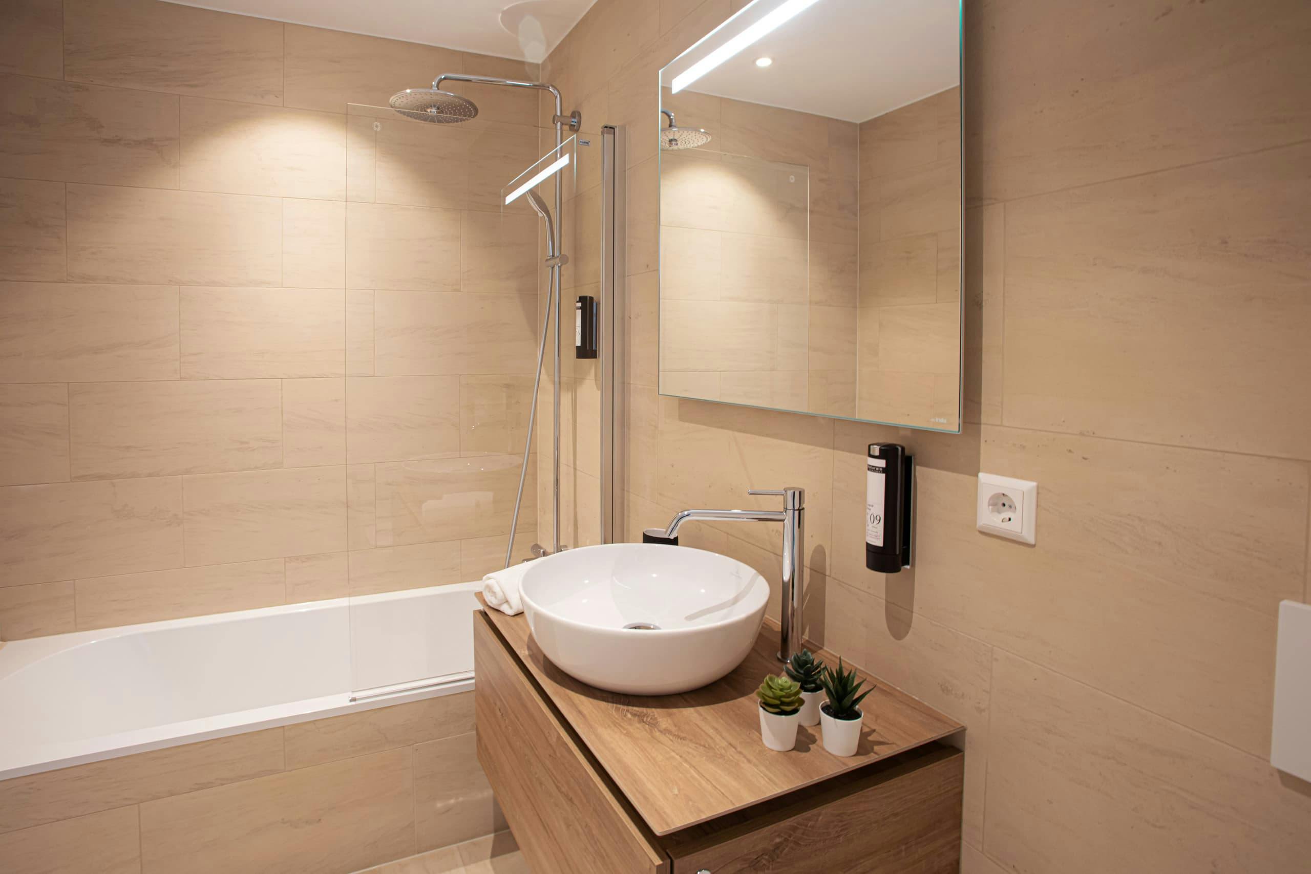 Bathroom with a bath and a sink. Above the sink, there is a cabinet with mirror doors. Towels and soap are provided.