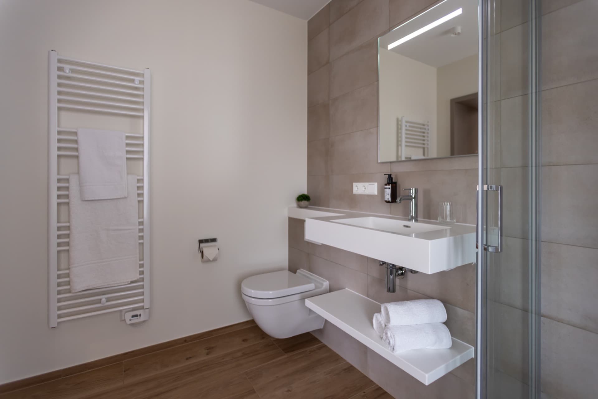 En-Suite Bathroom with walk-in shower, heating radiator, toilet, and sink.
Above sin,k there is a big mirror. Toiletries and towels are provided.