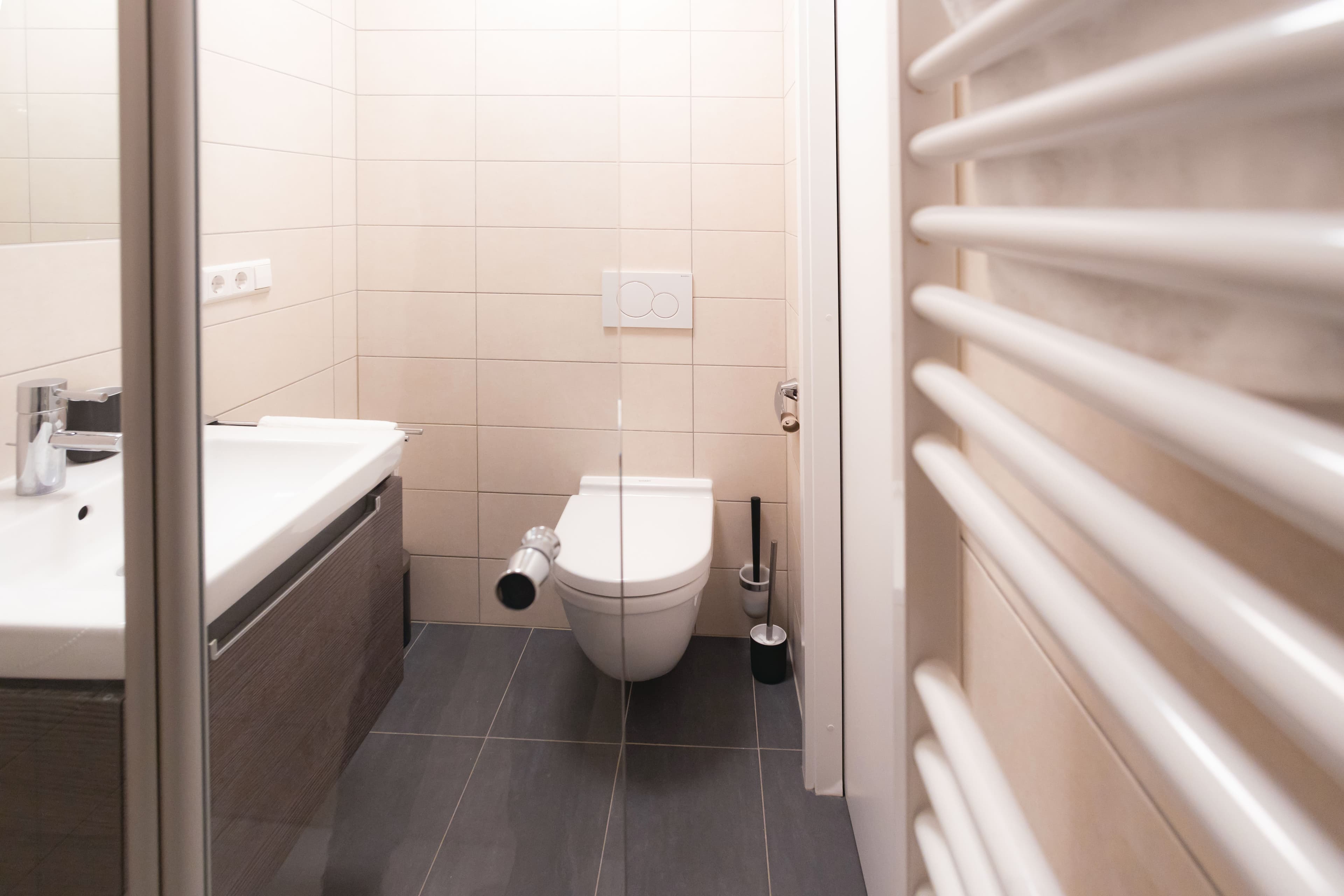 Toilet with a white sink next to it. A heating radiator and all amenities are included.