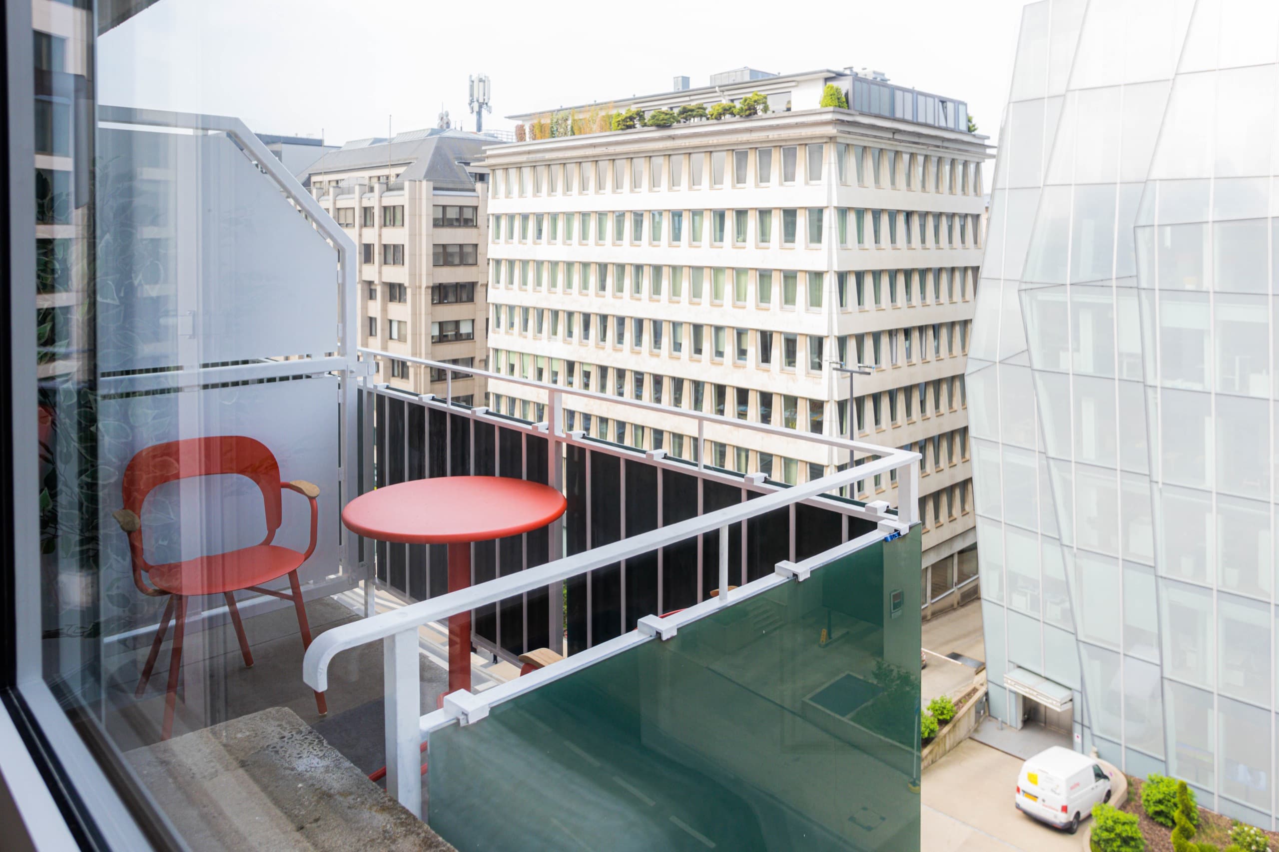 Balcony with a round red table and one red chair. View overlooking the city buildings.
