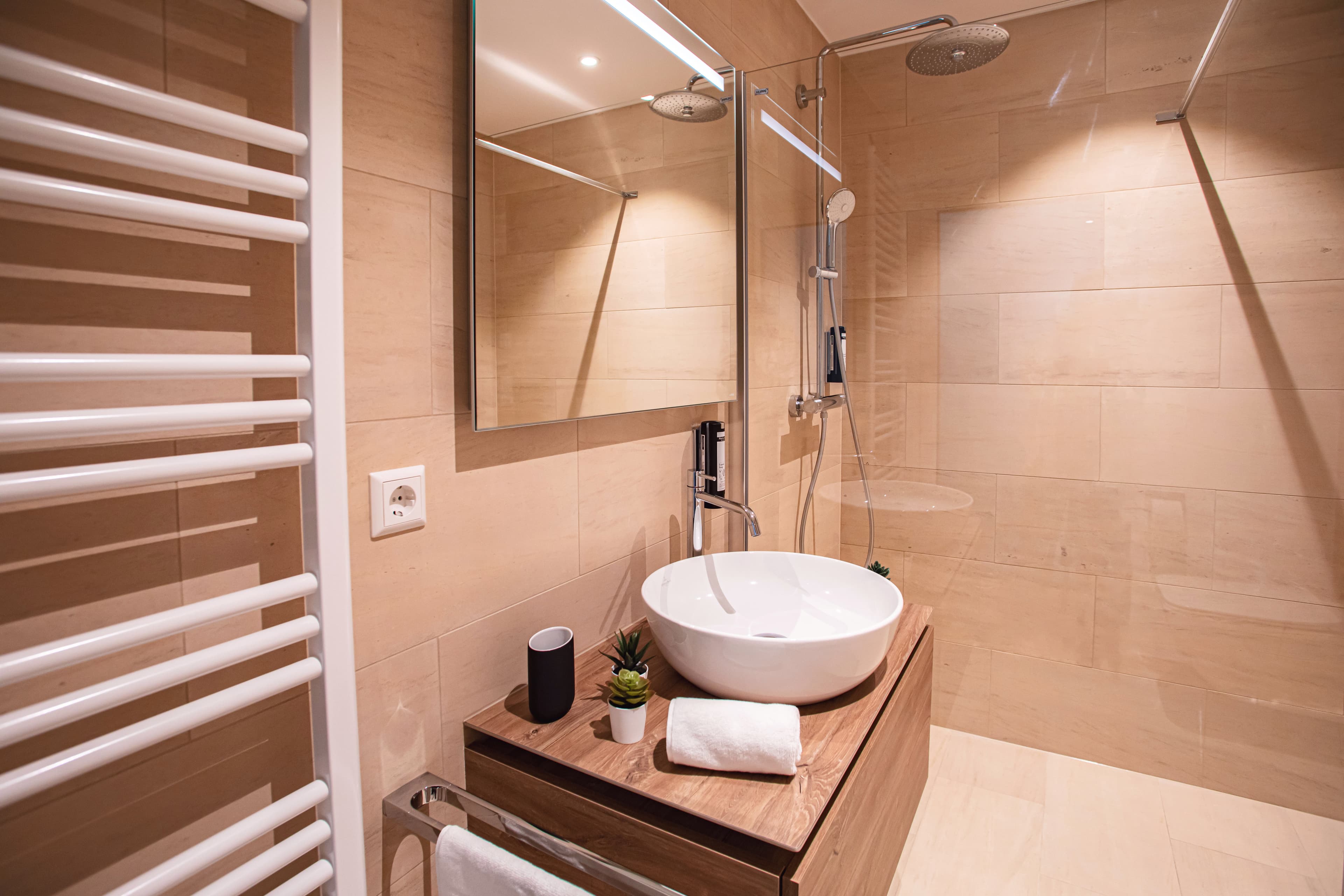 Bathroom with walk-in shower, a white sink, and a heating radiator. Above the sink, there is a mirror. All amenities included.