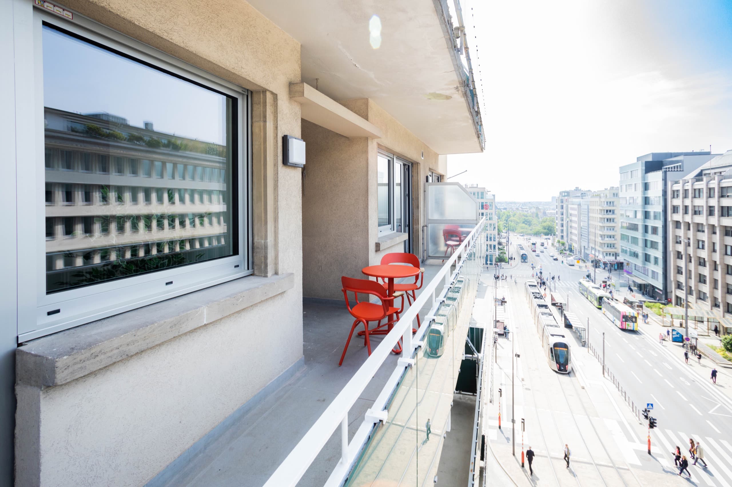 Balcony view with a red round table and two red chairs. It offers city overview.