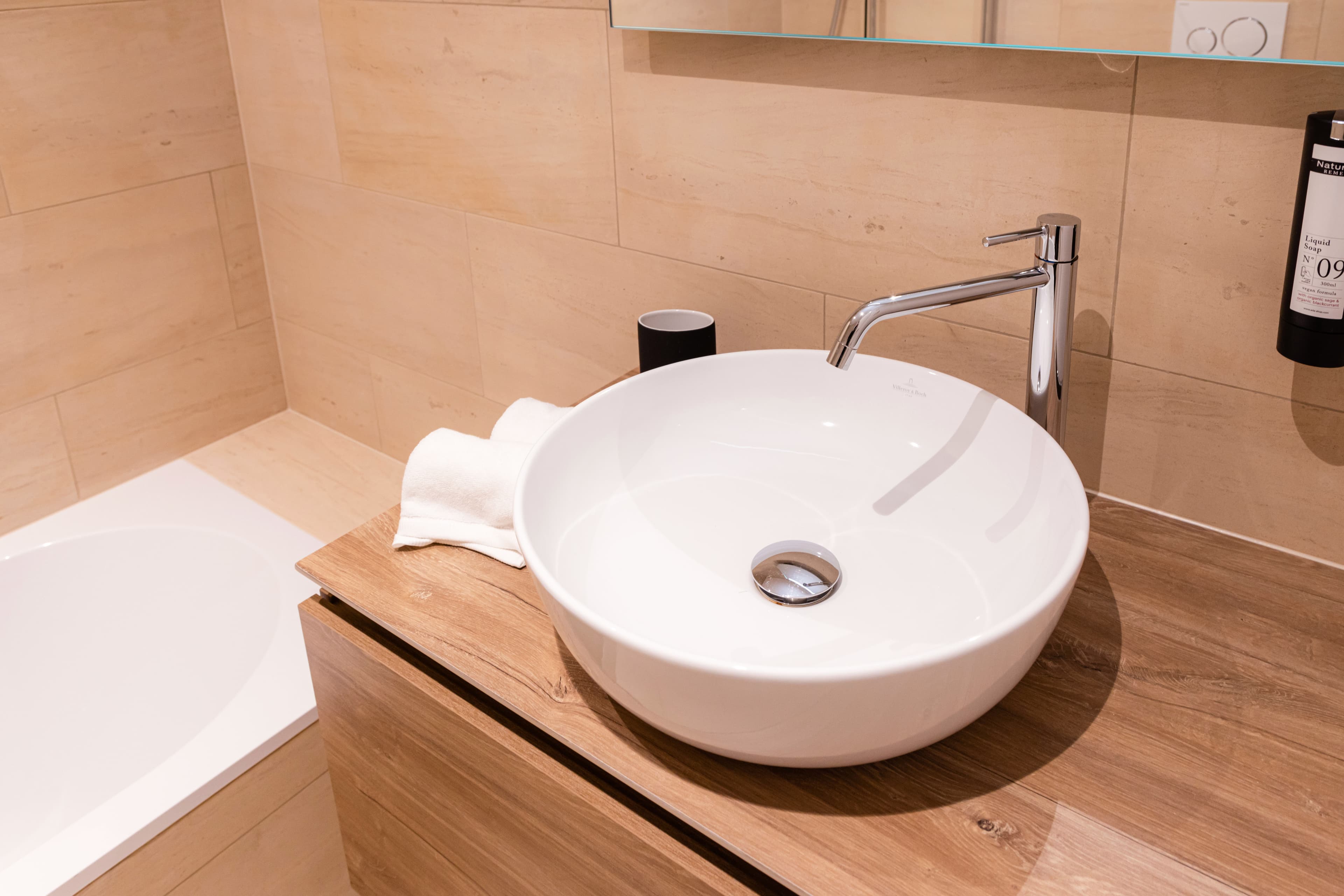 Bathroom with bath and white sink next to it. Above the sink there is a cabinet with mirror doors, towels and soap are provided.