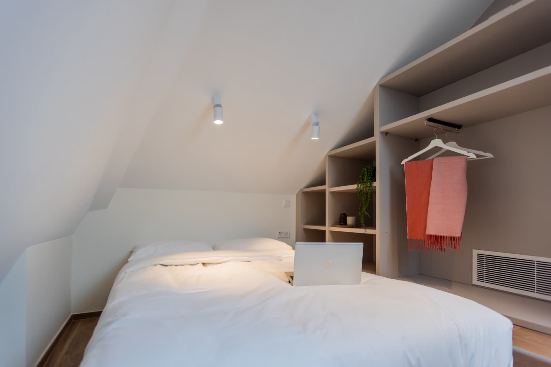 Close-up image of mezzanine bedroom for rent in Cessange House. It depicts a double bed with white cotton linens, on the right there is storage space and drawers. Above the bed there are 2 lamps