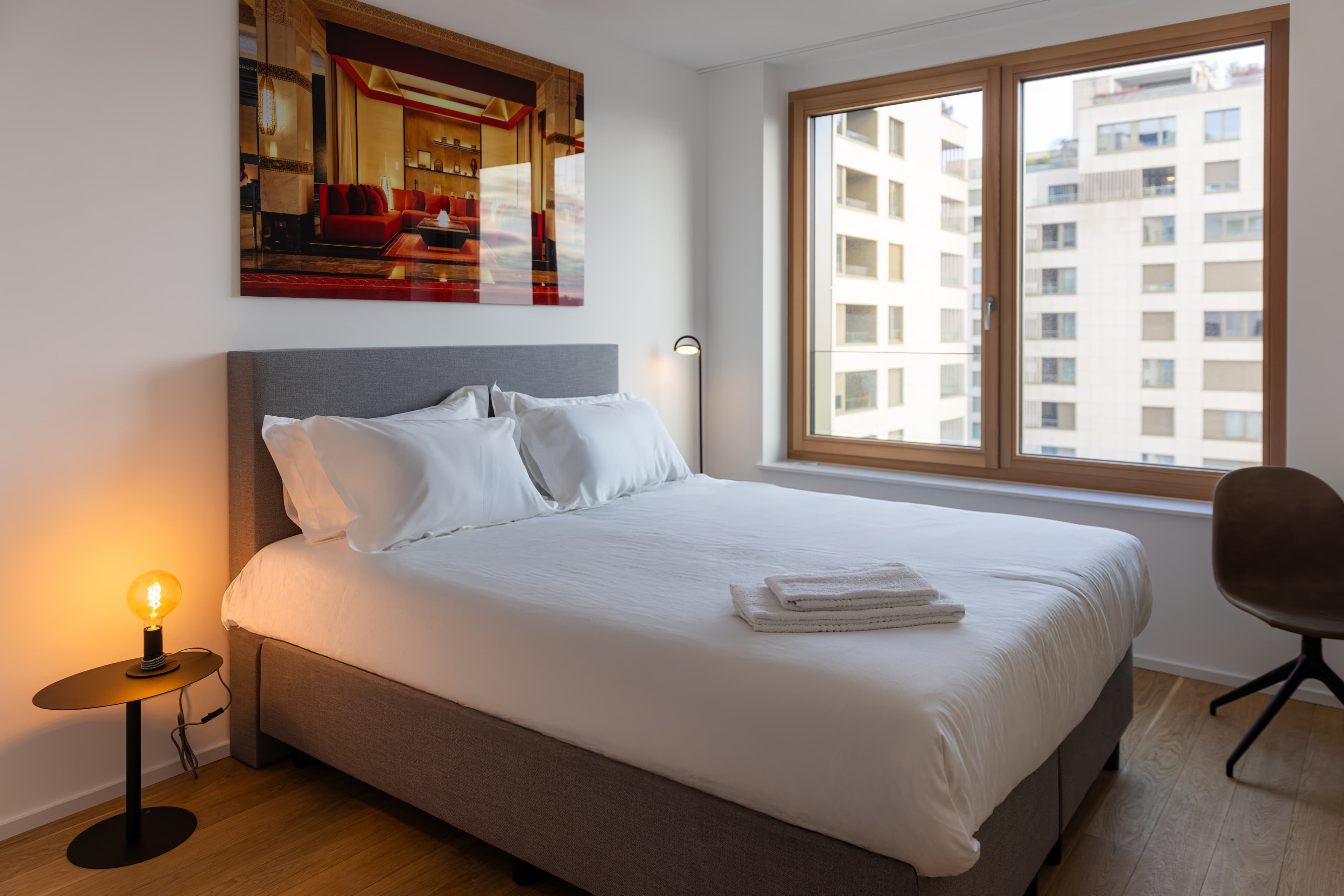 Overview of a bedroom with a king-size bed, a nightstand with a lamp on top. The bed has high-quality linens and plush pillows.