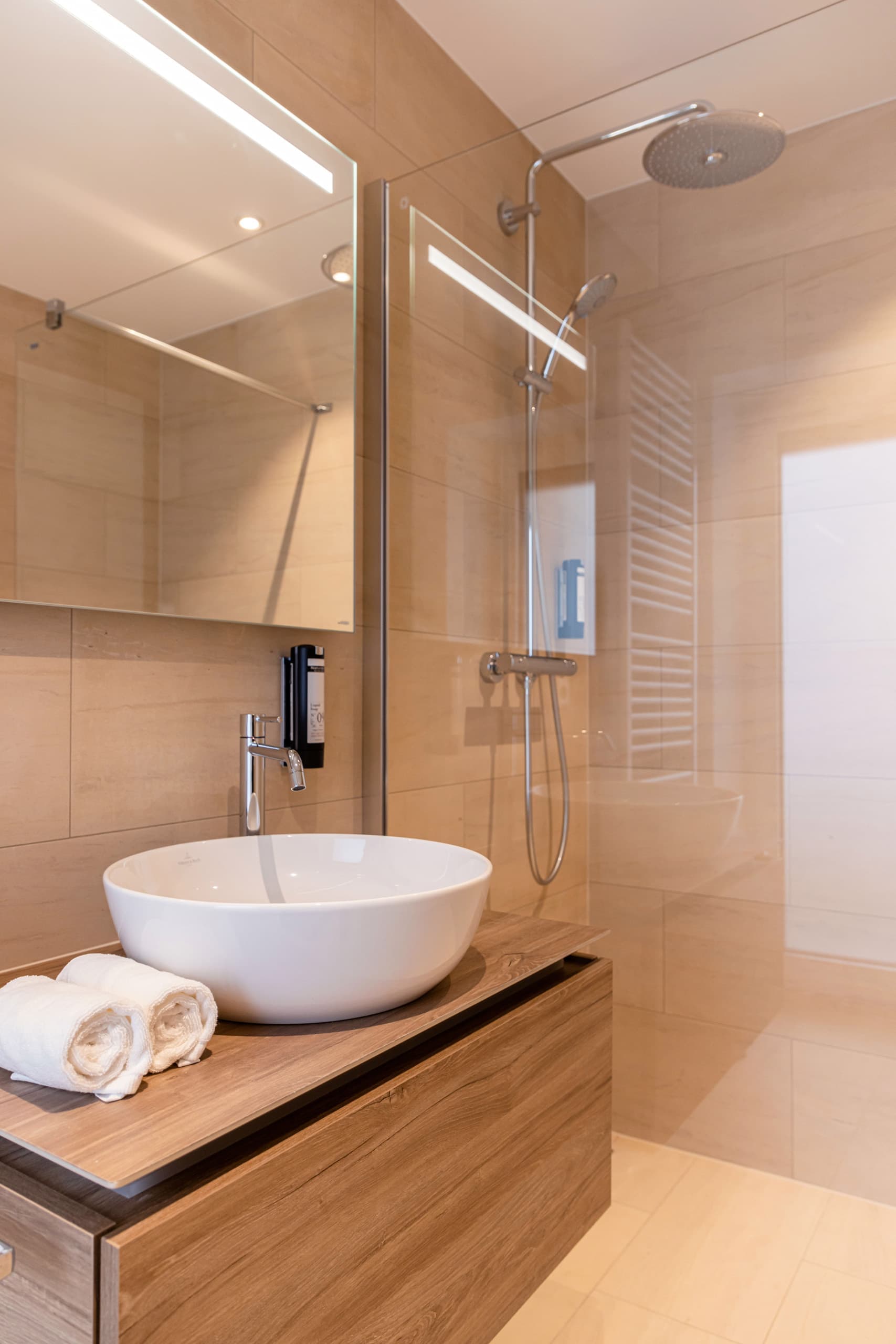Bathroom with shower cabin and sink on its left. Above the sink, there is a cabinet with mirror doors. Towels and soap are provided.