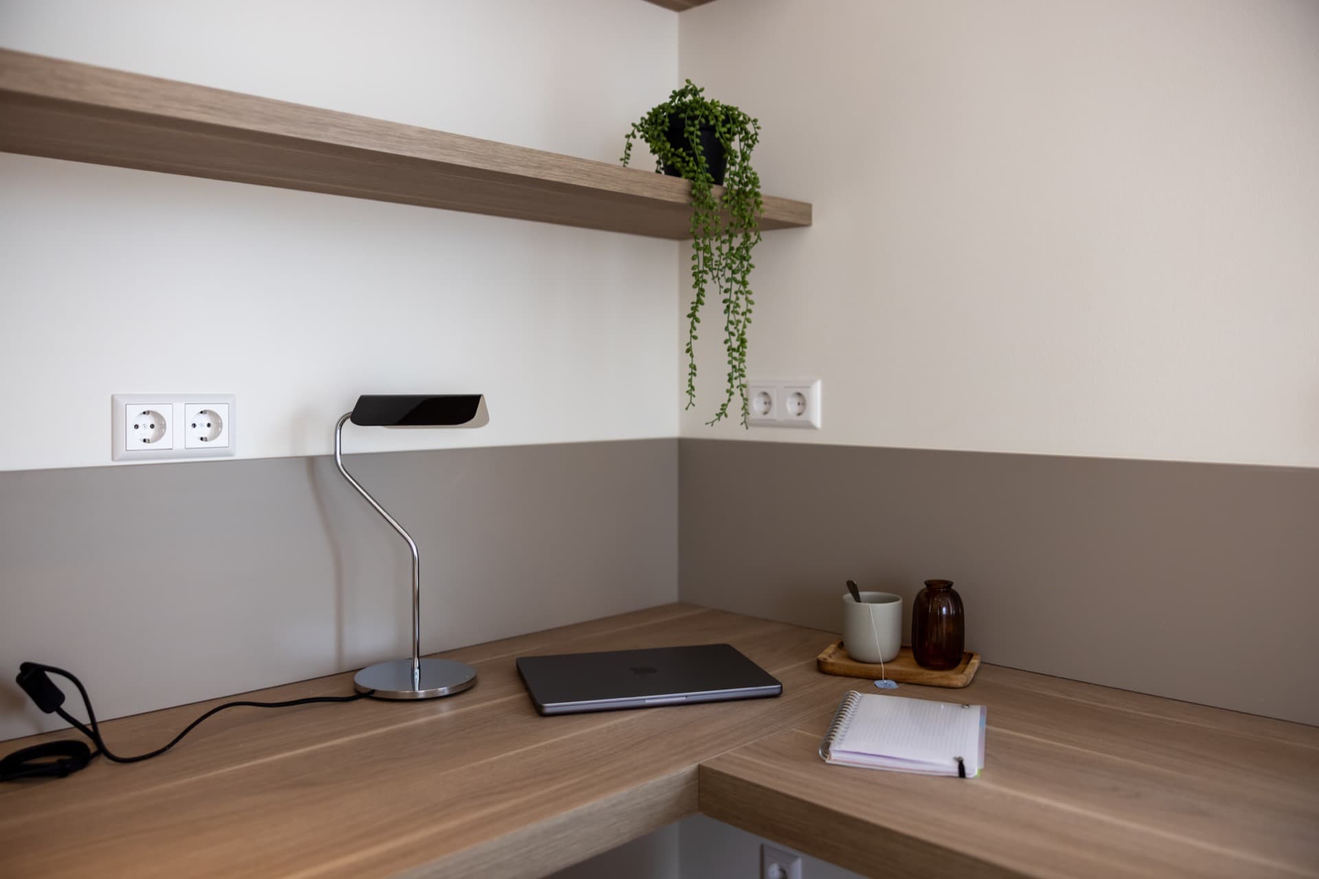 Close-up image of the working area including a desk with a lamp, a small vase with flower and a coffee mug.
Plugs are just in front of the desk.