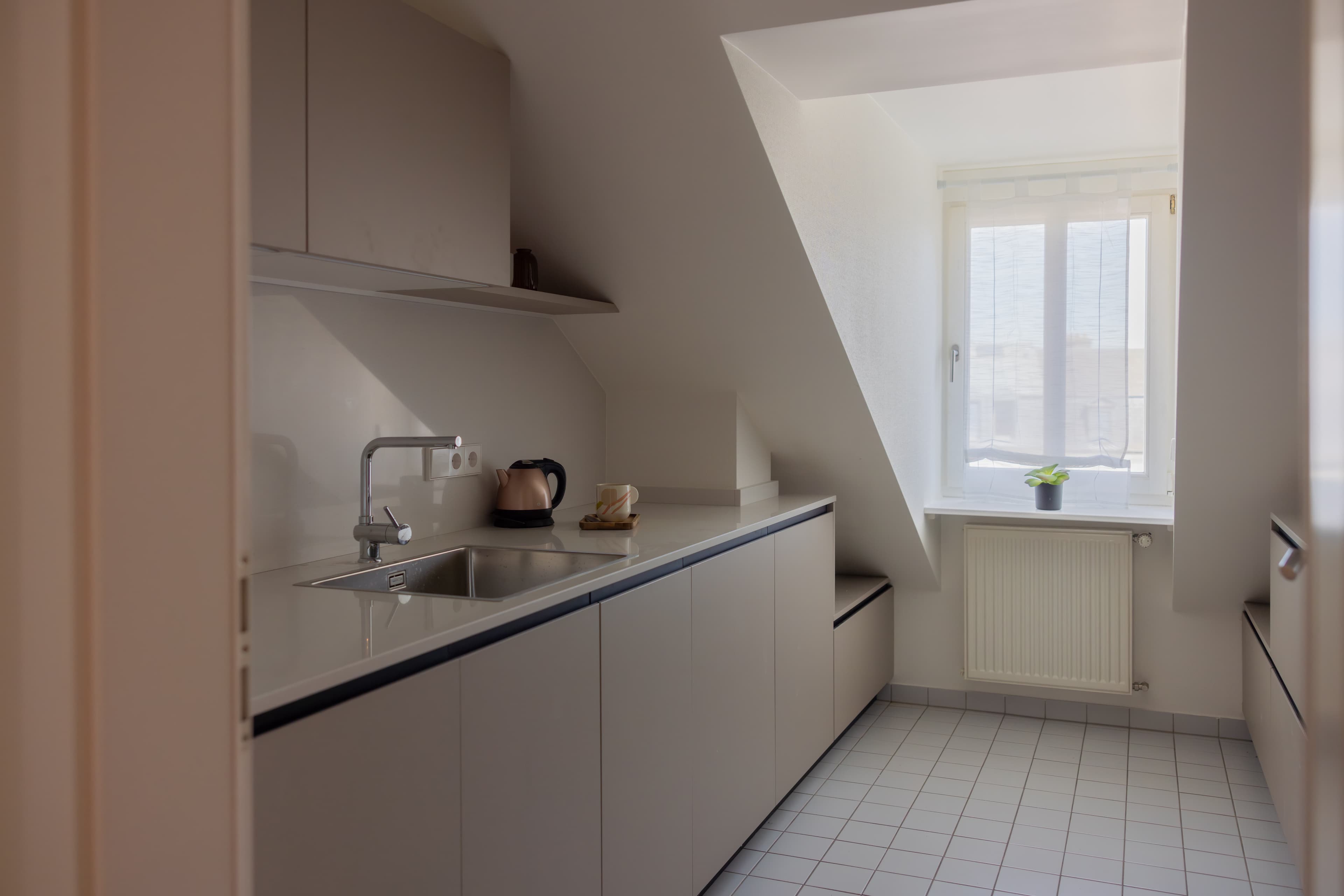 In the kitchen, there are countertops and utilities, beige furniture, and a large window. Under the window there is a heating radiator.