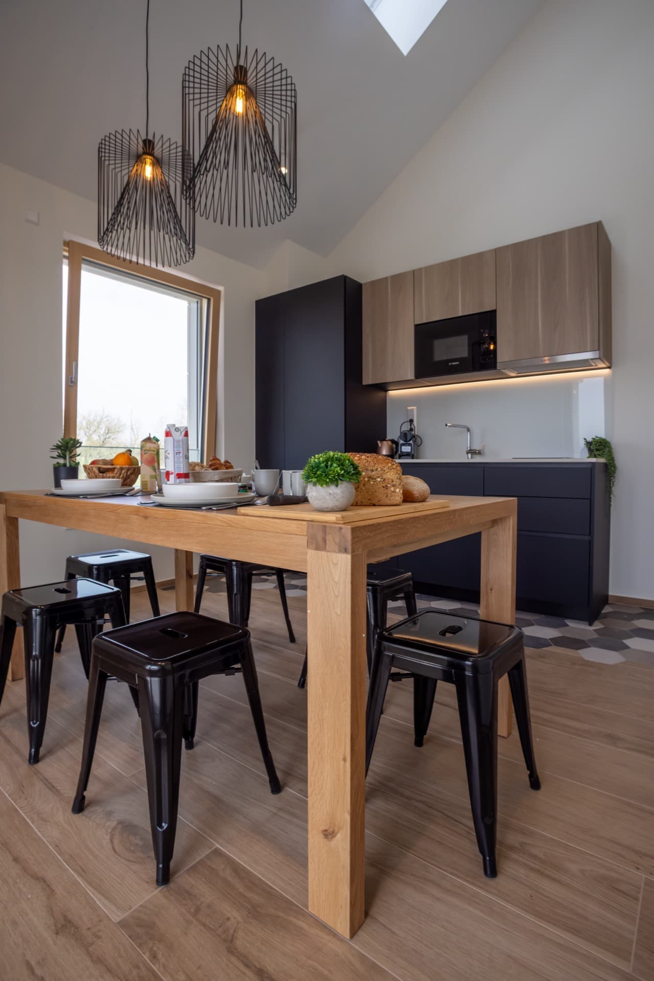 Tall wooden table with tall chairs. A fridge and freezer are provided along with a coffee machine and kettle. Storage spaces are above the kitchen